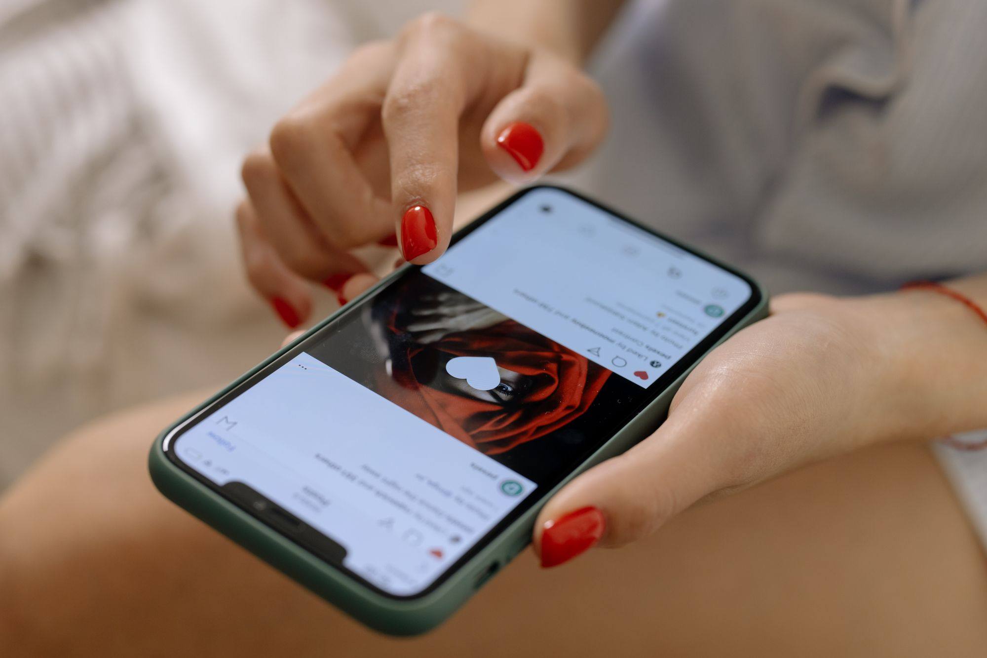 Mano de mujer con las uñas pintadas de rojo dando un doble toque a una publicación en el móvil, con un corazón sobre la imagen